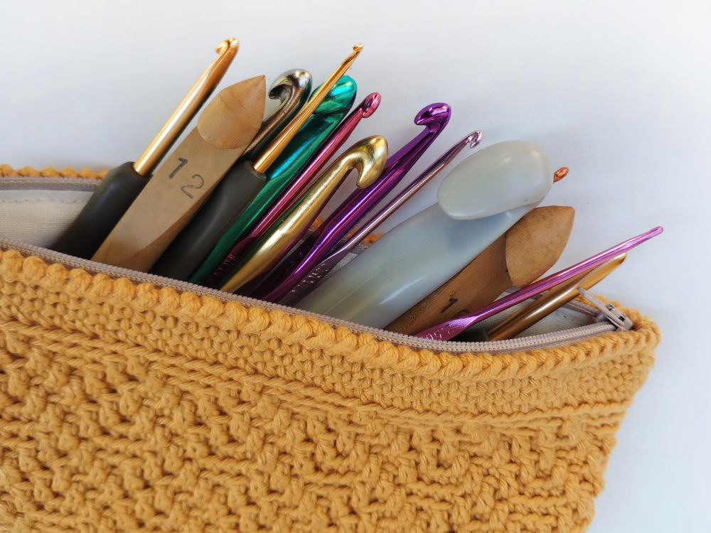 Estojo amarelo feito em crochê mosaico com uma coleção de agulhas de crochê de diversos tamanhos, formatos e materiais.